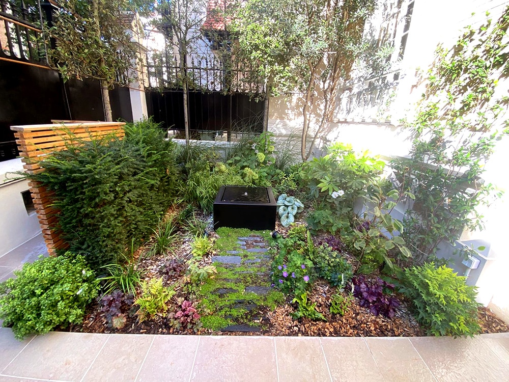 Onde verdoyante : jardin d'accueil en ville. Fontaine, pierres de comblanchien, menuiserie sur mesure, arbres en rideaux.